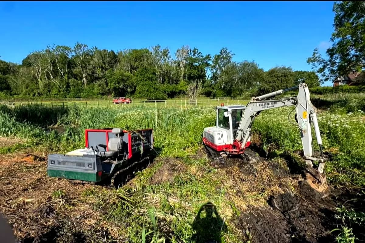 Excavator and tracked dumper at the overgrown edge of the pond